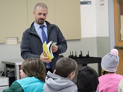 The principal opens a book that he prepares to read to students.
