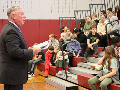 The assembly member holds a book in his hands as he speaks with students.