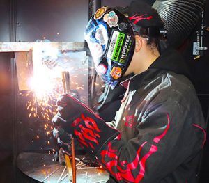 Student wearing protective helmet and gloves holds a welding.