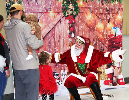 Santa greets a child with open arms and a smile as parents look on