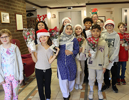 A group of students hold poinsettias and smile at the camera