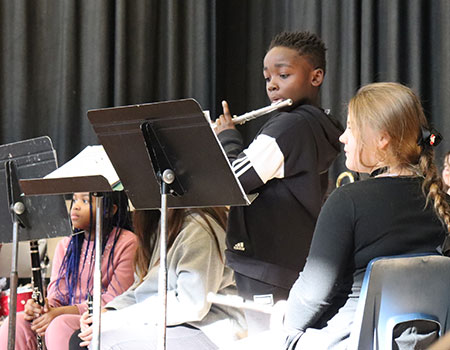 A student plays a flute solo as other band musicians sit nearby watching