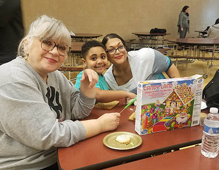 A child and family sit together and prepare materials to build a gingerbread house