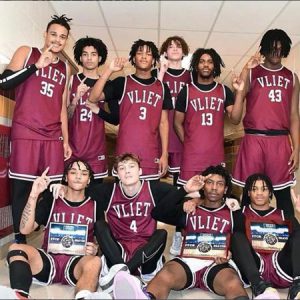 Members of the boys basketball team gather together, some sitting and others standing, to smile for the camera. 