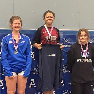 Watervliet wrestler stands in the center of the podium with two wrestlers on either side. All three wear medals. 