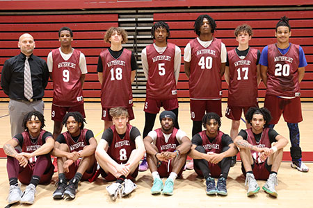 Varsity basketball coach stands with team in front of bleachers