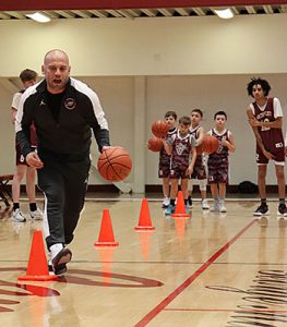 Basketball coach demonstrates skills drill as CYO and varsity players watch