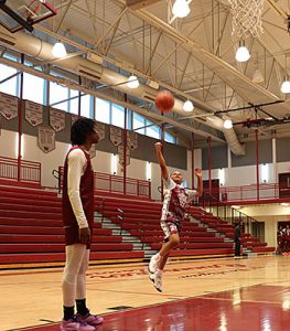 Varsity player stands beneath net as CYO player practices a lay up