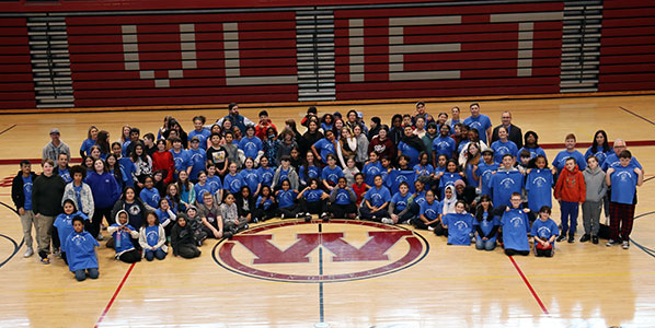 Sixth grade students, teachers, staff and administrators most dressed in blue gather in the gym to honor student