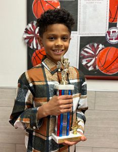 Spelling bee champion holds trophy and smiles at the camera