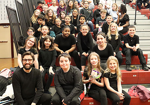 The entire drama club and adviser sit in the bleachers and smile for the camera 