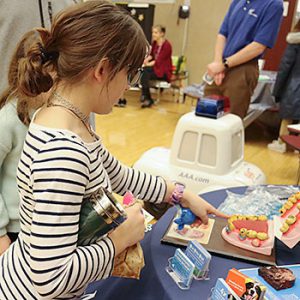 A student points to a plastic model of teeth with tobacco stains that on a table display promoting smoking cessation