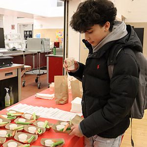 Student holds a smoothie in one hand and picks up a plate with vegetables and dip with the other hand