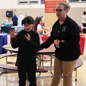 A student wears impaired vision goggles and tries to catch a ball as the Stop DWI presenter stands nearby