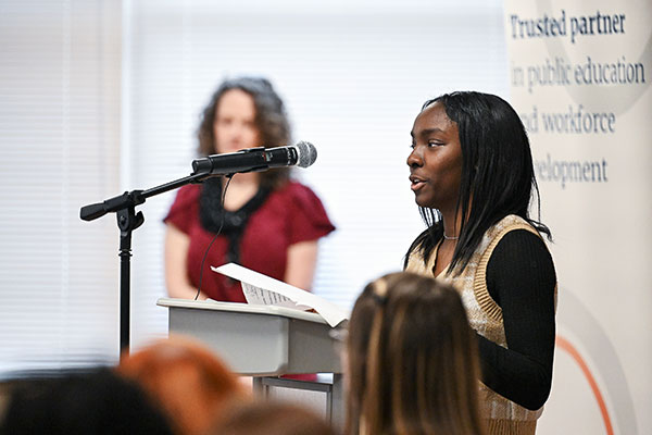Student stands at podium in front of microphone looking out at audience