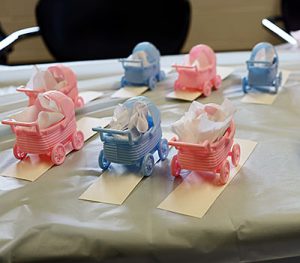Tiny pink and blue plastic baby carriages with white tissue paper peeking from inside are lined up on a desk.