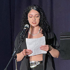 A student speaks into a microphone and reads from a piece of paper.