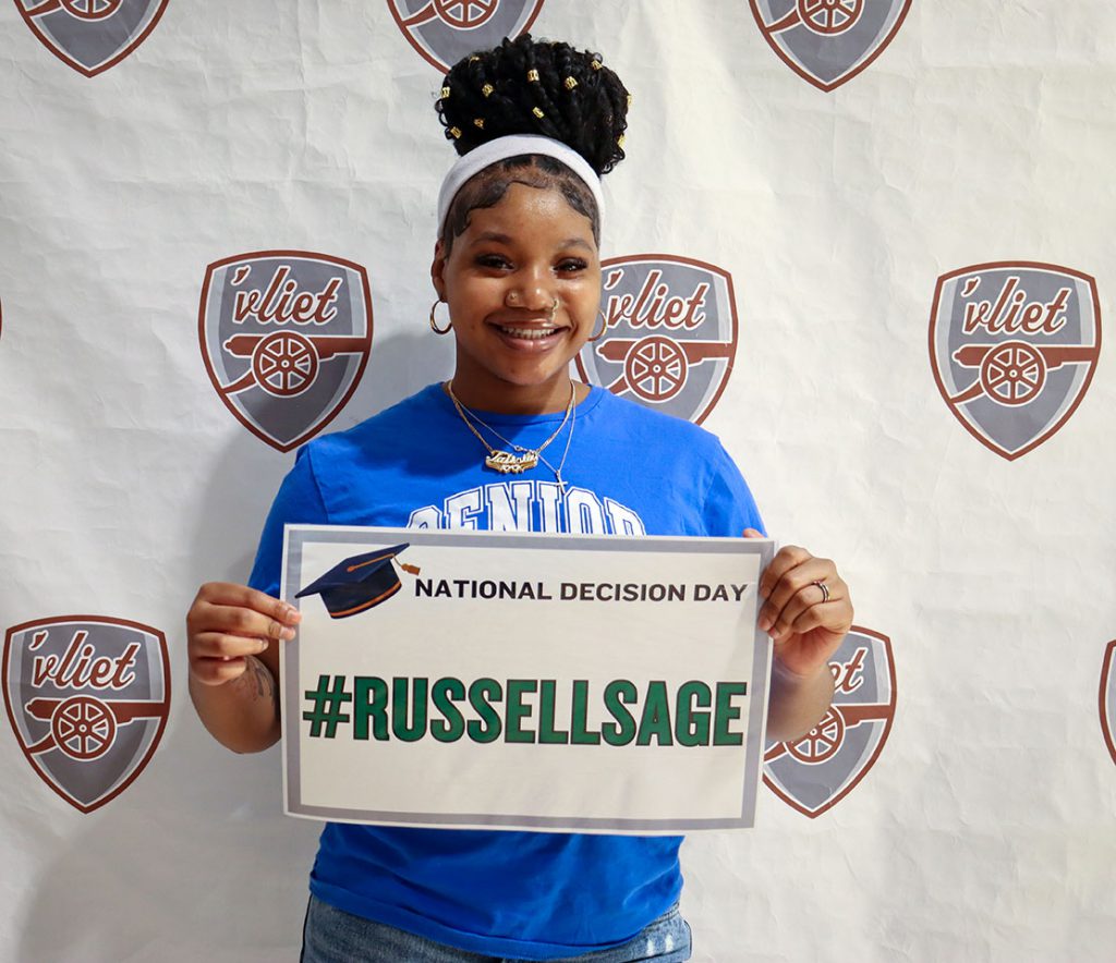 A member of the Class of 2025 holds a Russell Sage College sign and smiles 