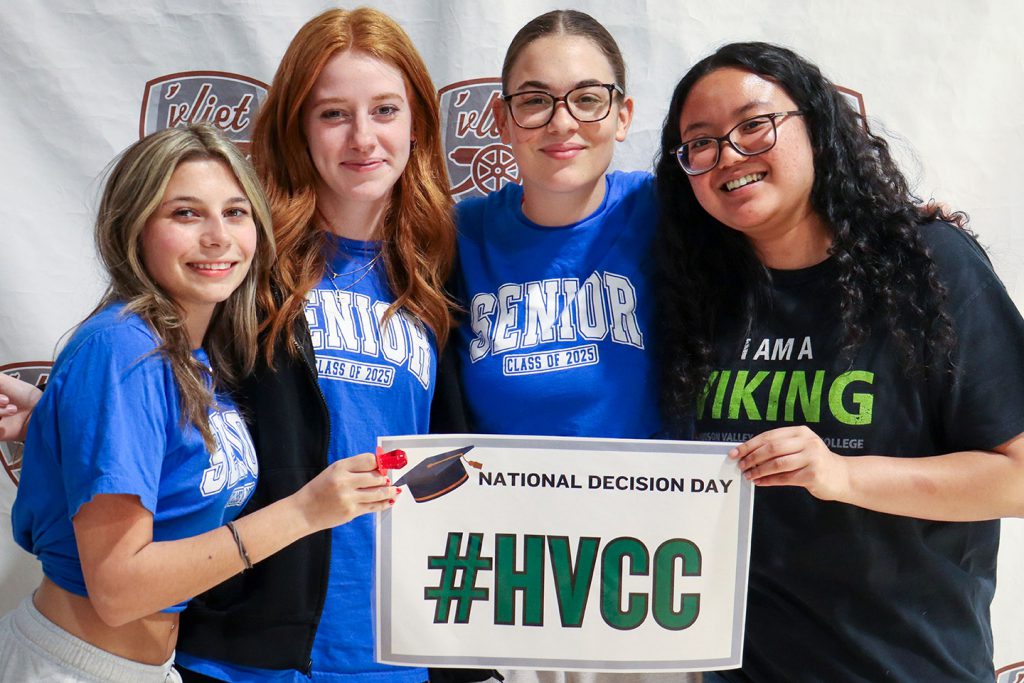 Four members of the Class of 2025 hold an HVCC sign and smile 