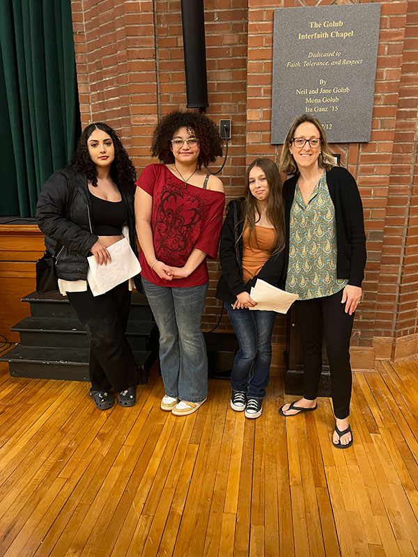 A teacher stands with three students in front of a brick wall near the stage at the Capital Region Poetry Slam