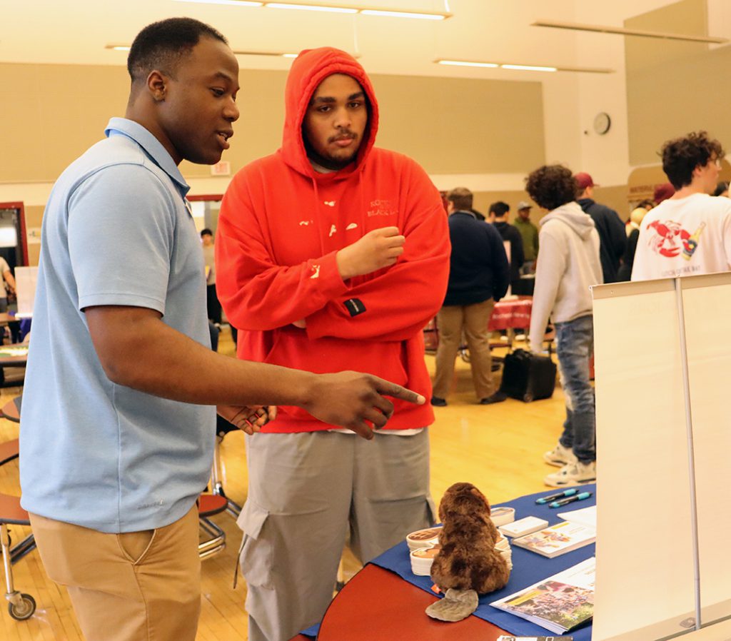 Student dressed in orange hoodie talks with a college representative