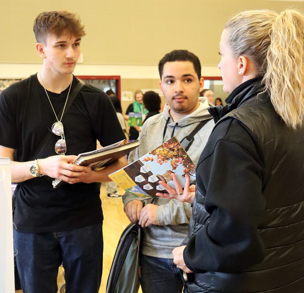 Two students hold literature while talking with a college representative