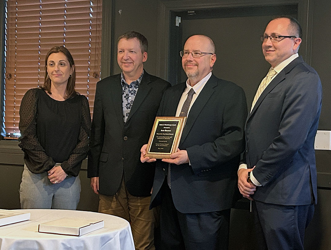 Teacher holds award as superintendent and high school principal stand beside.