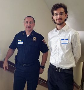 A student stands next to the police chief at the top of the stairs in City Hall