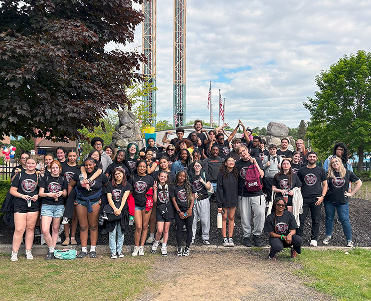 Large group of band and chorus students stand in front of a tall amusement park ride at music festival