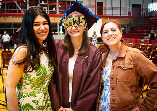 A graduate stands in the center as two high school teachers stand on either side
