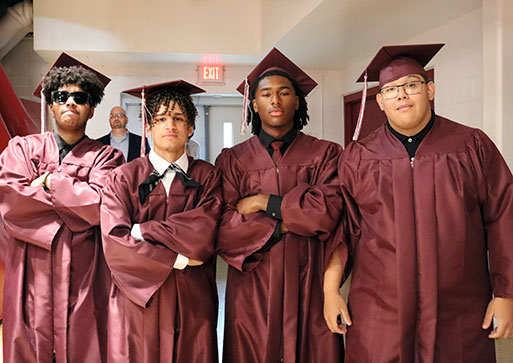 Four graduates stand in a group dressed in caps and gowns