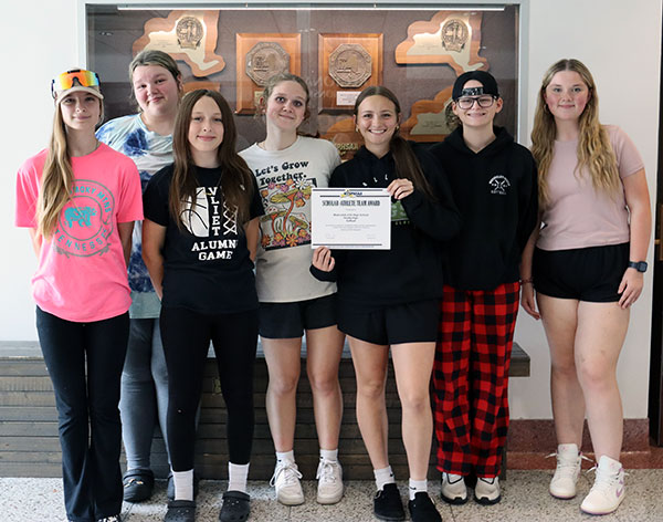members of the varsity softball team stand together holding a certificate designating Scholar Athlete Team status