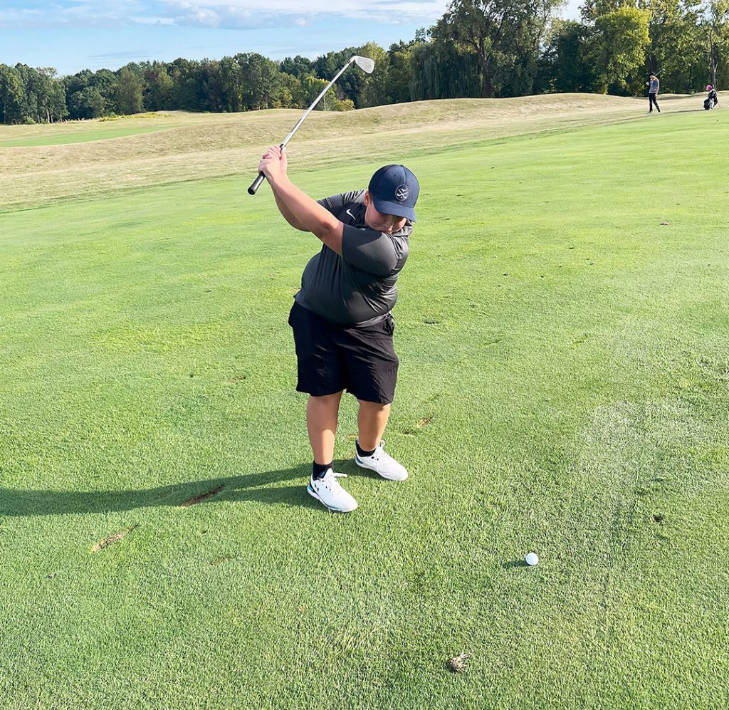 Member of golf team in swing stance ready to tee off