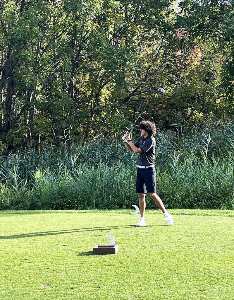 Member of golf team watches ball after teeing off