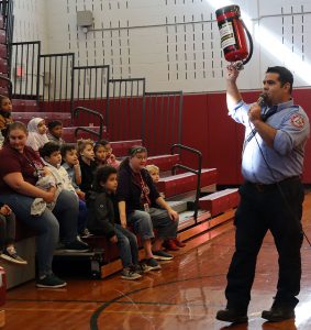 A Watervliet firefighter  raises a fire extinguisher over =head and reminds students about fire safety tips