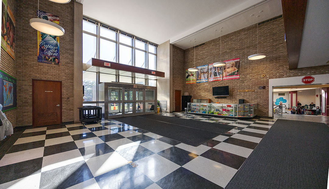 School lobby in current condition shows doors to main entrance, high ceiling and small area for school store to the right