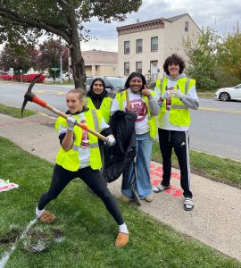 A small group of students stand ready with tools to plant trees.