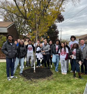 Eighteen character ed students stand together near a freshly planted tree