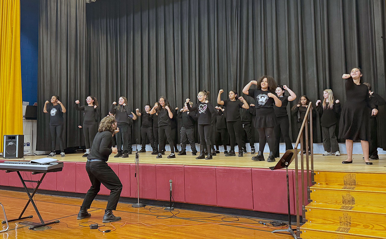 Large group of students dressed in black perform a dance on stage