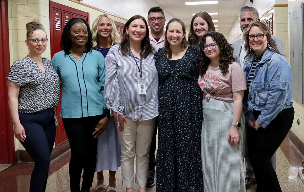 Ten smiling educators stand together in a group in a hallway at Watervliet Junior Senior High School