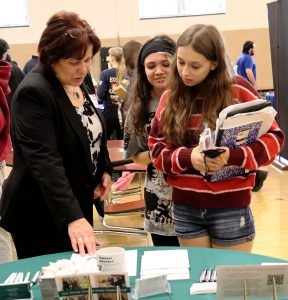 Two students speak with a local professional who is pointing to brochure on table