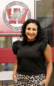 New assistant principal stands in hallway near banner with Watervliet City Schools logo
