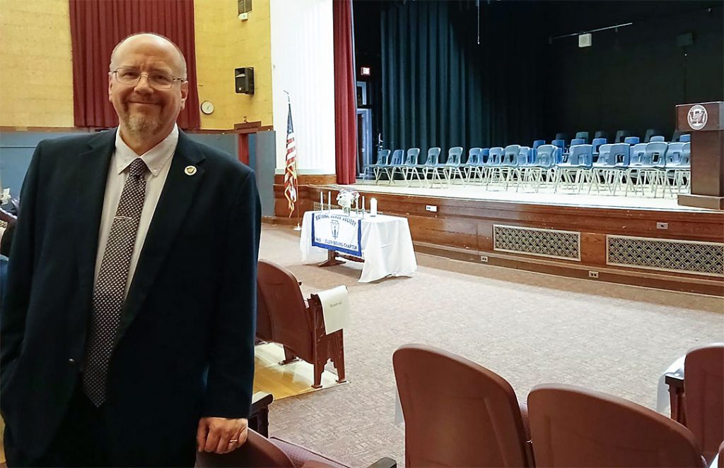 Teacher stands in front of stage that has been set up with chairs for induction ceremony
