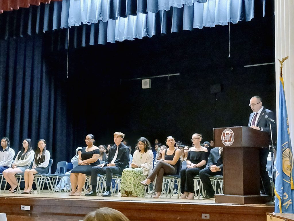 Superintendent stands at podium delivering the oath to National Honor Society inductees