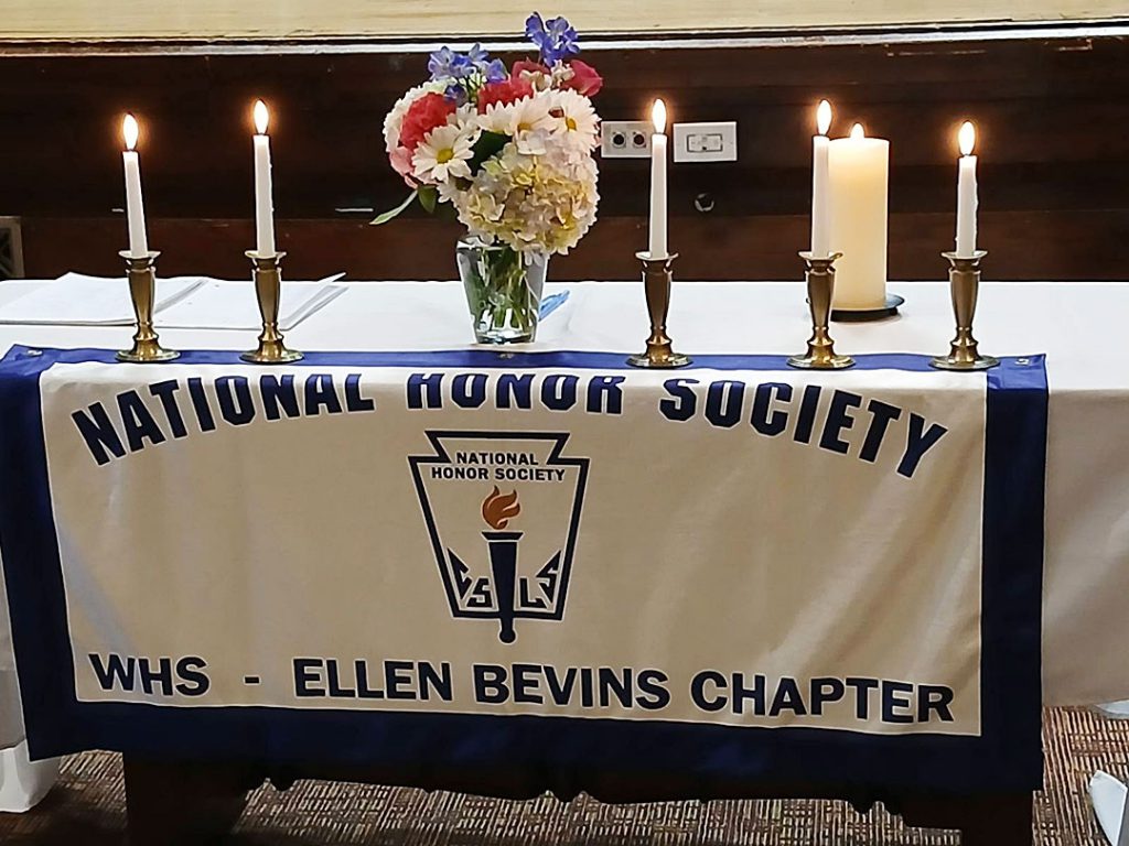 A table with National Honor Society banner is set with flowers and candles