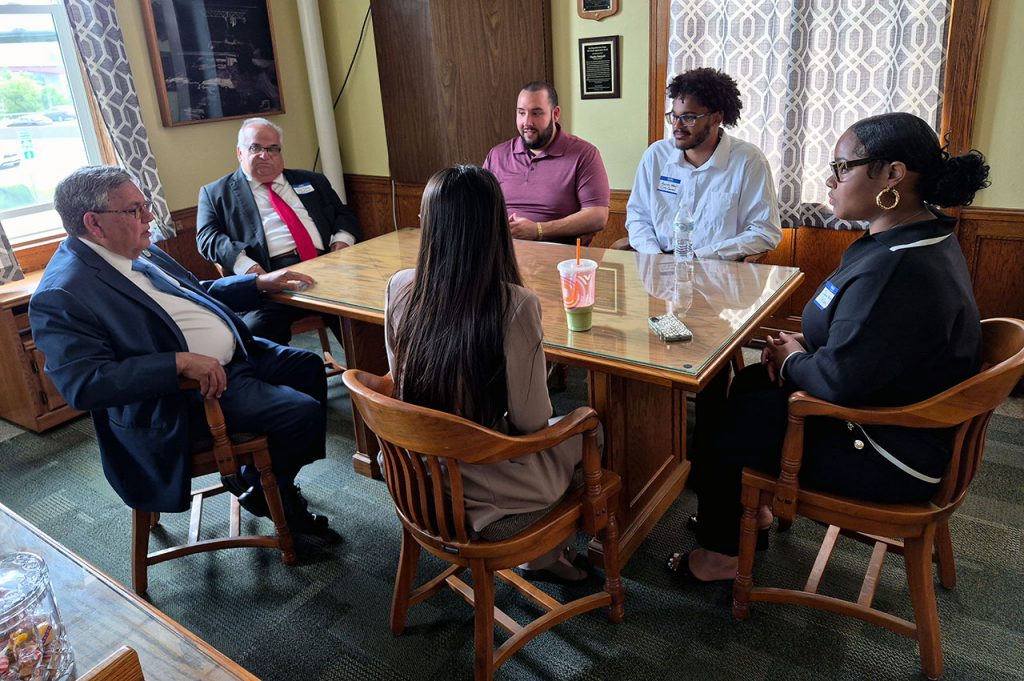 Three students in mayor's office seated at table talking with the mayor and council members