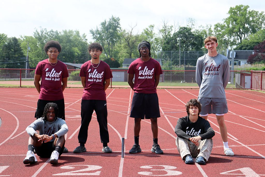 Four athletes stand and to athletes sit at the finish line on the high school track