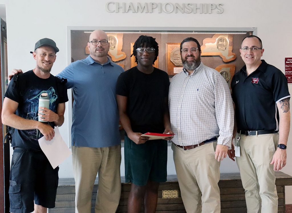Scholarship award winner stands with his teachers, the high school principal and the superintendent of schools