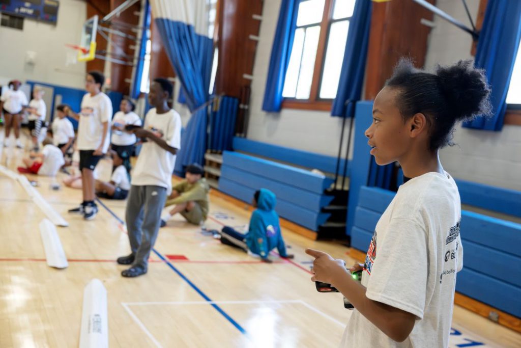 A student holds a remote controller and steers his car around the racetrack