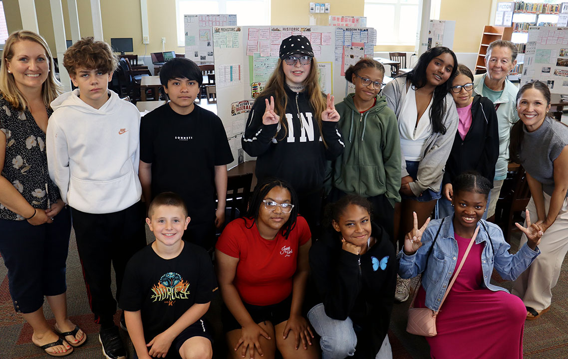 Students and teachers in the summer travel program stand together in the school library